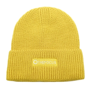Detail of yellow knit beanie featuring a stitched THEFOCUS logo patch on a folded cuff