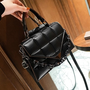 Black quilted handbag with chain strap and triangular buckle shown in a lifestyle setting