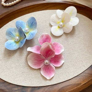 Close-up of fabric flower hair clips in blue, white, and pink with pearl centers