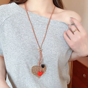 Detail of a tiered heart pendant necklace with brown leather cords on a grey shirt