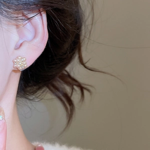 Close-up of elegant flower stud earrings with small pearls on model's earlobe