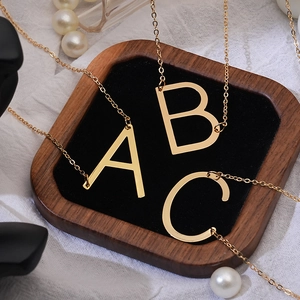 Detailed view of polished gold A, B, and C letter pendants on fine stainless steel chains