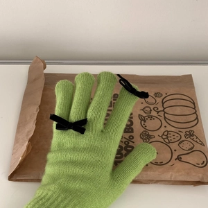 Close-up of green knit glove with black bow detail on fingers over paper bag