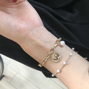 Vintage gold-layered bracelet featuring a relief coin pendant and white pearls on a model