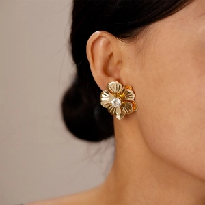 Détail d'une boucle d'oreille fleur dorée avec cristal central portée par un mannequin