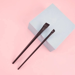 Dual ultra-fine eyeliner and eyebrow makeup brushes with sleek black handles on pink background
