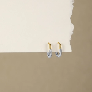 Detail of two-tone gold and silver U-shaped hoop earrings on textured paper
