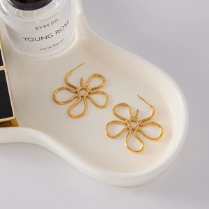 Close-up of golden floral hollow earrings displayed on a white ceramic tray with a prop bottle