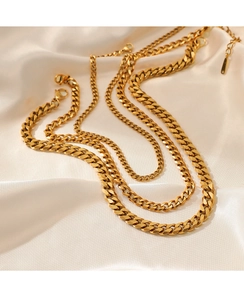 Detailed view of three layered gold Cuban chain necklaces on elegant beige silk fabric