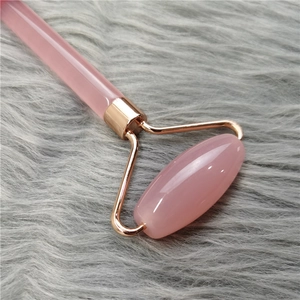 Close-up of pink quartz roller with rose gold frame on a grey textured surface