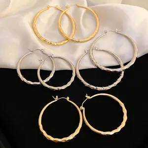 Textured gold and silver hoop earrings with geometric lattice pattern on white silk