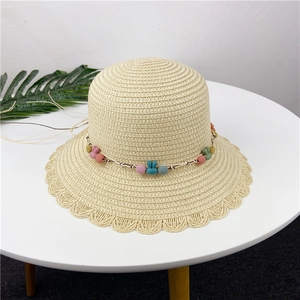 Close-up of beige straw hat with colorful rabbit beads and scalloped brim edge
