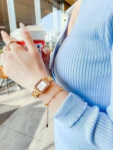Close-up of a gold square watch with crystal bezel worn on wrist with elegant bracelets