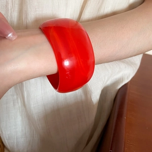 Close-up of a wide red resin bangle worn by a model on a beige fabric background