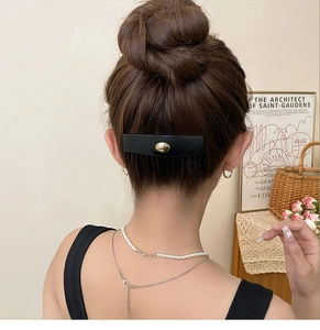 Close-up of vintage black acrylic oval hair clip with gold metal H logo on bun hairstyle