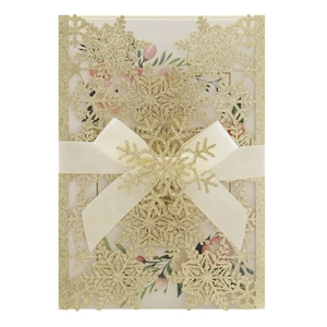 Detail of laser-cut snowflake invitation with gold glitter and beige satin ribbon bow