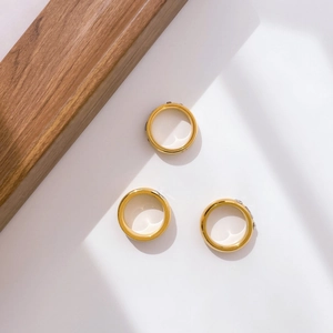 Three wide golden polished rings arranged on a white background with natural window shadows