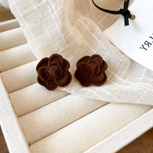 Macro shot of dark brown flocked camellia stud earrings on a cream velvet jewelry tray