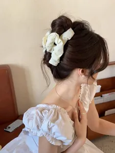 Close-up of a cream pleated fabric hair scrunchie styled on a classic bun hairstyle