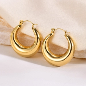 Chunky gold-plated hollow crescent hoop earrings on elegant silk and stone background