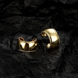 Macro view of wide gold ear cuffs with polished finish and beaded edges on black background