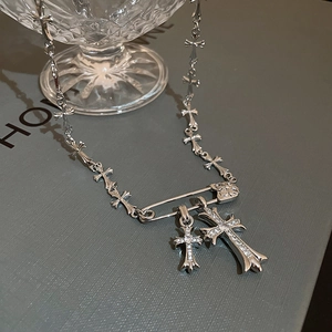 Macro shot of silver safety pin necklace featuring zircon crosses on a grey display box