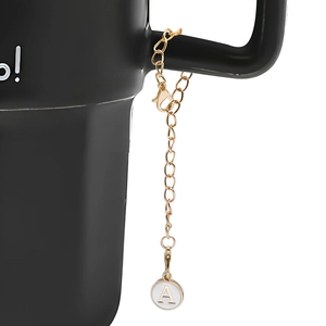 Detail of golden initial A charm with white enamel on a black coffee mug handle