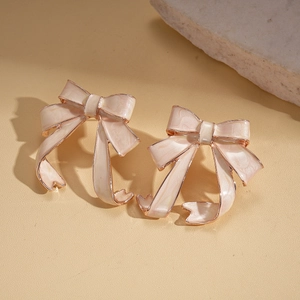 Detail of pink bow earrings with pearlescent enamel finish on warm beige stone texture