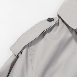 Detail shot of light gray trench coat shoulder strap with black four-hole button
