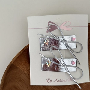 Detail of silver rectangular hair clips with heart-shaped gems on a white display card