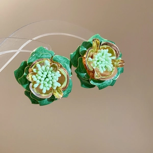 Détail des boucles d'oreilles fleurs vert foncé avec bords dorés et centre en relief