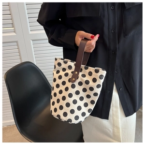 Detailed close-up of a white polka dot canvas bucket bag with brown leather handles