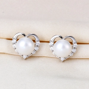 Macro detail of heart-shaped S925 silver earrings with pearls and crystal pavé on silk