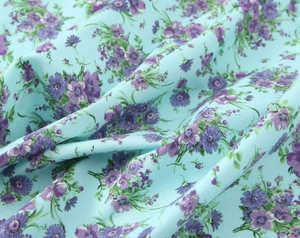 Close-up of light blue poplin fabric with dense purple floral print and smooth texture