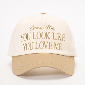 Detailed close-up of brown embroidered text on a cream and khaki cotton baseball cap