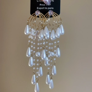 Macro detail of dangling pearl tassels and teardrop pendant on gold earrings