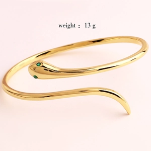 Detail of gold snake bangle featuring sparkling green gemstone eyes and 13g metal weight