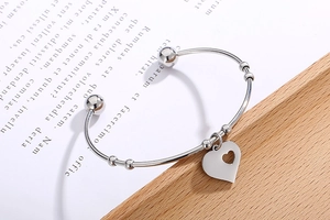 Detail of silver heart charm on polished stainless steel open bangle bracelet