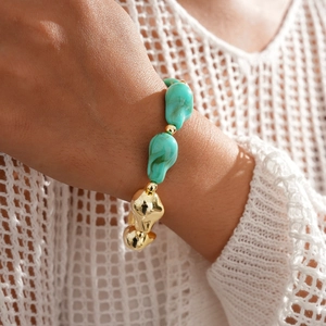 Détail de bracelet bohème avec perles irrégulières dorées et vert lagon sur le poignet d'un mannequin