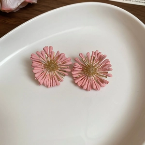 Detailed view of pink raffia daisy earrings on a white ceramic tray for beach vacations