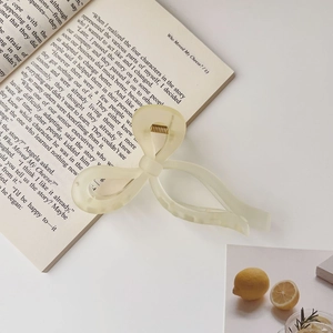 Detail of frosted cream bow hair claw clip on a stylish table with lemons and book