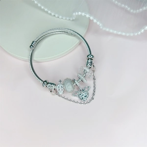 Silver beaded charm bracelet with heart wings and crown pendants on pink background