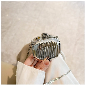 Mini silver chain bag with metallic ripple design held by hand for size reference
