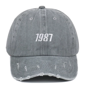 Detail of the 1987 embroidery and distressed brim on gray washed denim baseball cap
