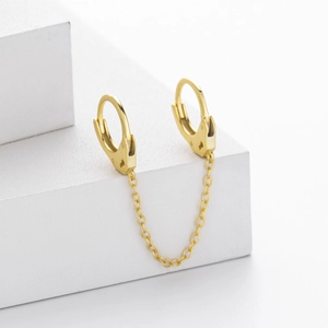 Detailed close-up of gold double-cuff chain earrings on a modern white display