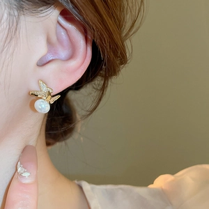 Close-up of butterfly stud earring with sparkling zircon and pearl on model ear