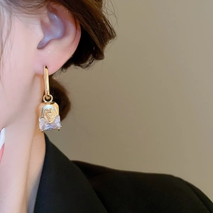 Close-up of gold-plated lion head earrings with square crystal pendant worn by model