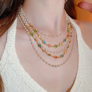 Close-up of layered necklace with white pearls and colorful gemstones on a gold chain