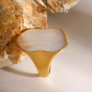 Macro shot of gold wide band ring with irregular white shell inlay against stone backdrop