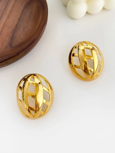 Detailed close-up of gold hollow woven sphere earrings on a minimalist wooden tray